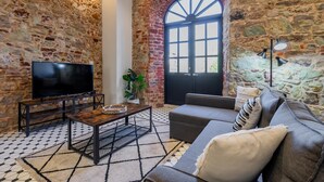 Un accogliente soggiorno con parete in pietra, una grande finestra ad arco, un televisore a schermo piatto, un divano e un tavolino da caffè.