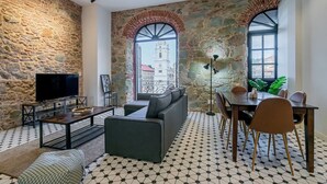 Una sala de estar moderna con paredes de piedra, un ventanal grande, un sofá, un televisor y un comedor.