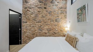 Un dormitorio con pared de piedra, una cama, un cuadro y una puerta.