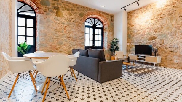 Amplia sala de estar con pared de piedra, un sofá, un televisor y una mesa de comedor con sillas.