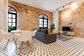 A spacious living area with a stone wall, a sofa, a TV, and a dining table with chairs. - w* | Polished 1BR in Plaza Catedral (Panamá)