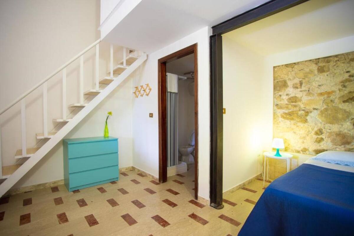 Ein Schlafzimmer mit einem Bett, einem Nachttisch, einer Lampe, einer Kommode und einer Treppe.