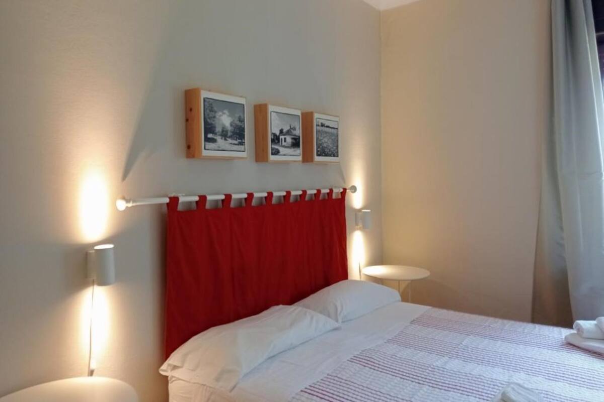 Ein Hotelzimmer mit einem Bett, einem roten Kopfteil, zwei Wandleuchten und drei gerahmten Bildern an der Wand.