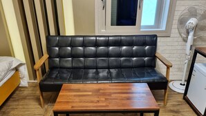 A black leather sofa with wooden armrests, a wooden coffee table, and a standing fan. - hwamyeong sky hotel (Busan)