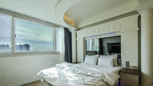 A modern hotel room with a large bed, a TV, and a city view. - hwamyeong sky hotel (Busan)