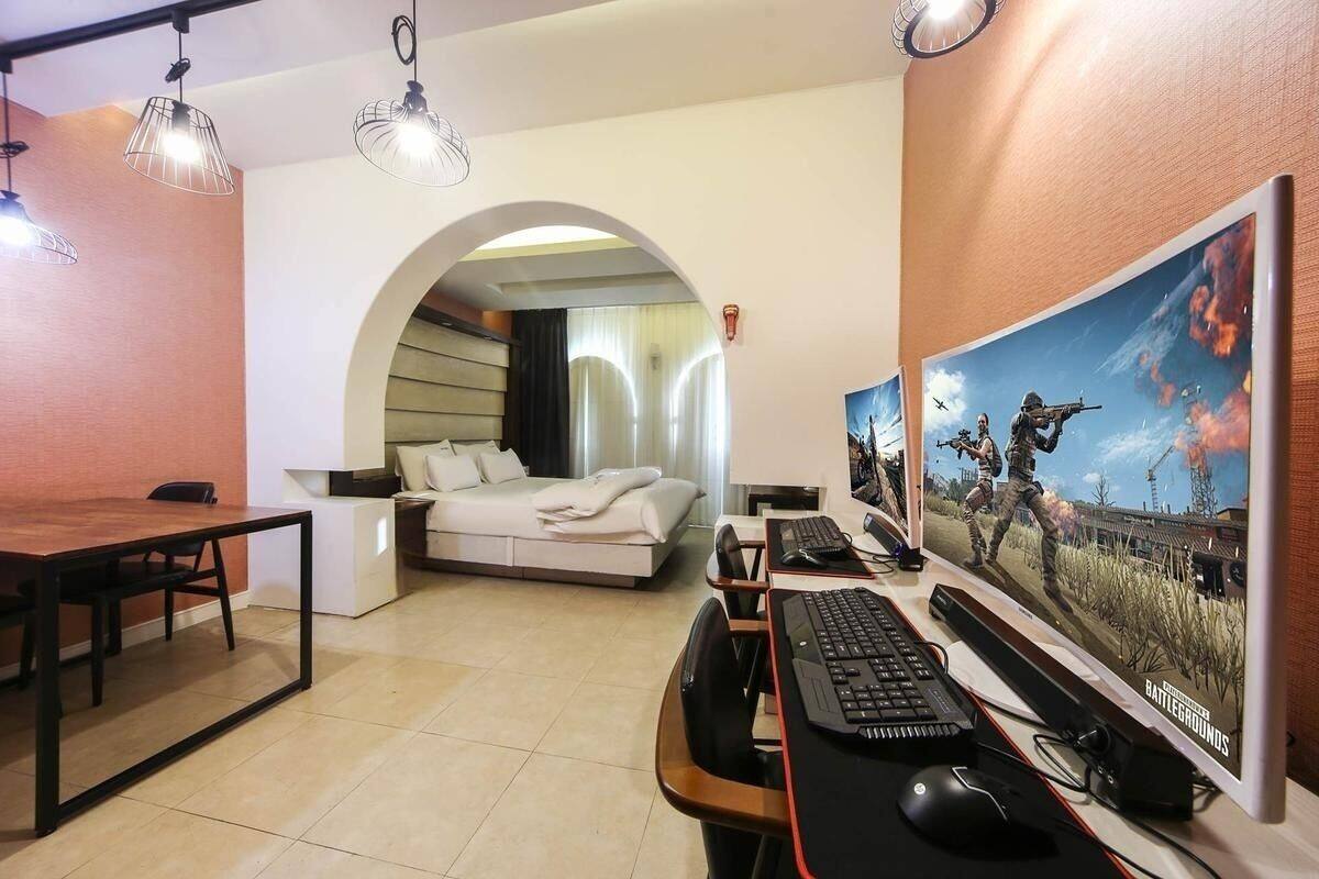 A hotel room with a bed, a desk with a computer, a chair, a table, and a large poster on the wall.