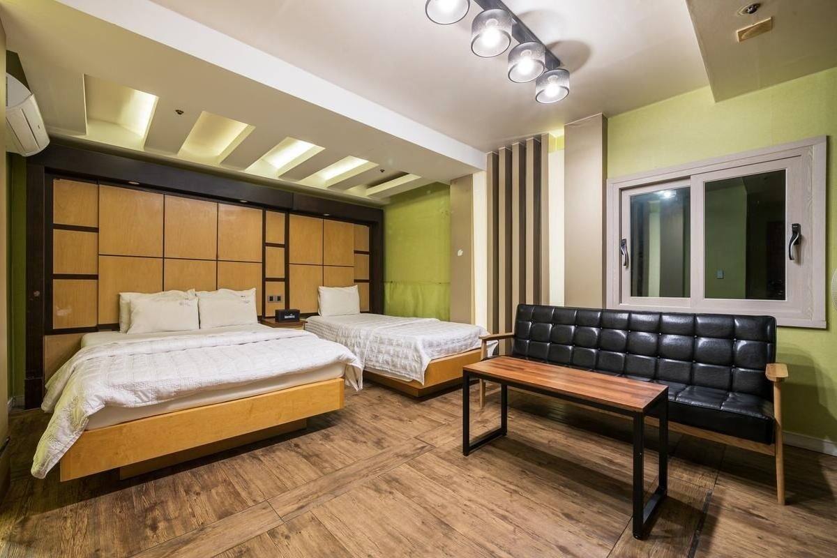 A bedroom with two beds, a bench, and a window.