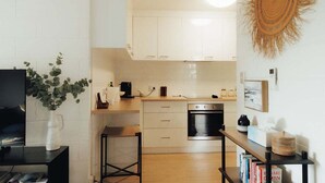 Et kompakt køkken med hvide skabe, indbygget ovn og et lille spiseområde med barstole.