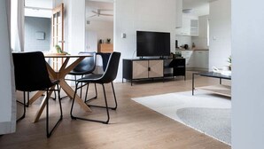En moderne stue med spiseplads, et fladskærms-tv og et køkken i baggrunden.