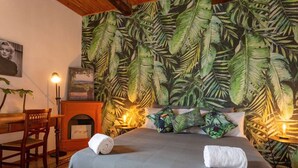 Ein Schlafzimmer mit Bett, Schreibtisch, Stuhl, Kamin und tropisch bebluteter Tapete.