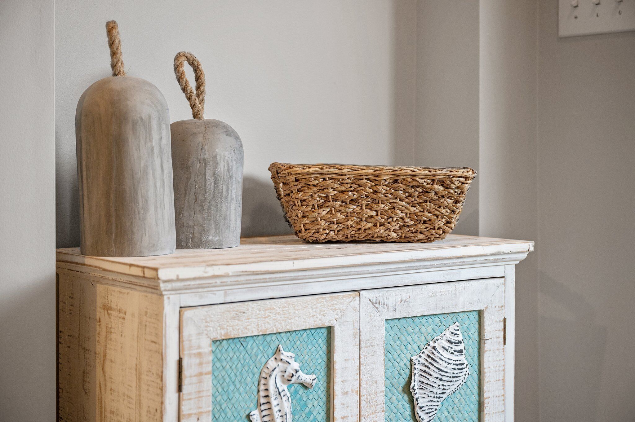 A rustic wooden cabinet with a woven basket and two cylindrical containers on top.