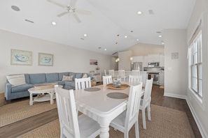 A dining area with a white table and chairs, a ceiling fan, recessed lighting, and a kitchen in the background.