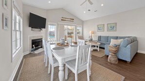 A spacious living room with a fireplace, a dining area, and a blue sofa. - Ocean Views. Clean! Pup Friendly. 2 Min Walk to the Beach. Beach Gear Included (Surf City)