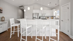 A modern kitchen with white cabinetry, a central island with bar stools, stainless steel appliances, and pendant lighting. - Ocean Views. Clean! Pup Friendly. 2 Min Walk to the Beach. Beach Gear Included (Surf City)