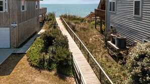 A wooden boardwalk leading to a beach with a view of the ocean. There are two buildings, one with a balcony and another with a deck. - Ocean Views. Clean! Pup Friendly. 2 Min Walk to the Beach. Beach Gear Included (Surf City)