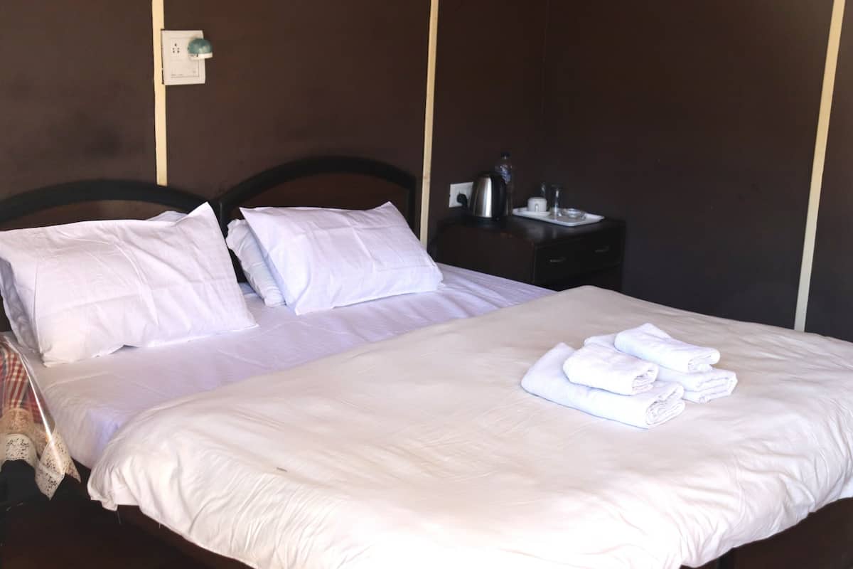 A neatly made bed with white linens and towels, a dark wooden headboard, and a small bedside table with a kettle and a glass.