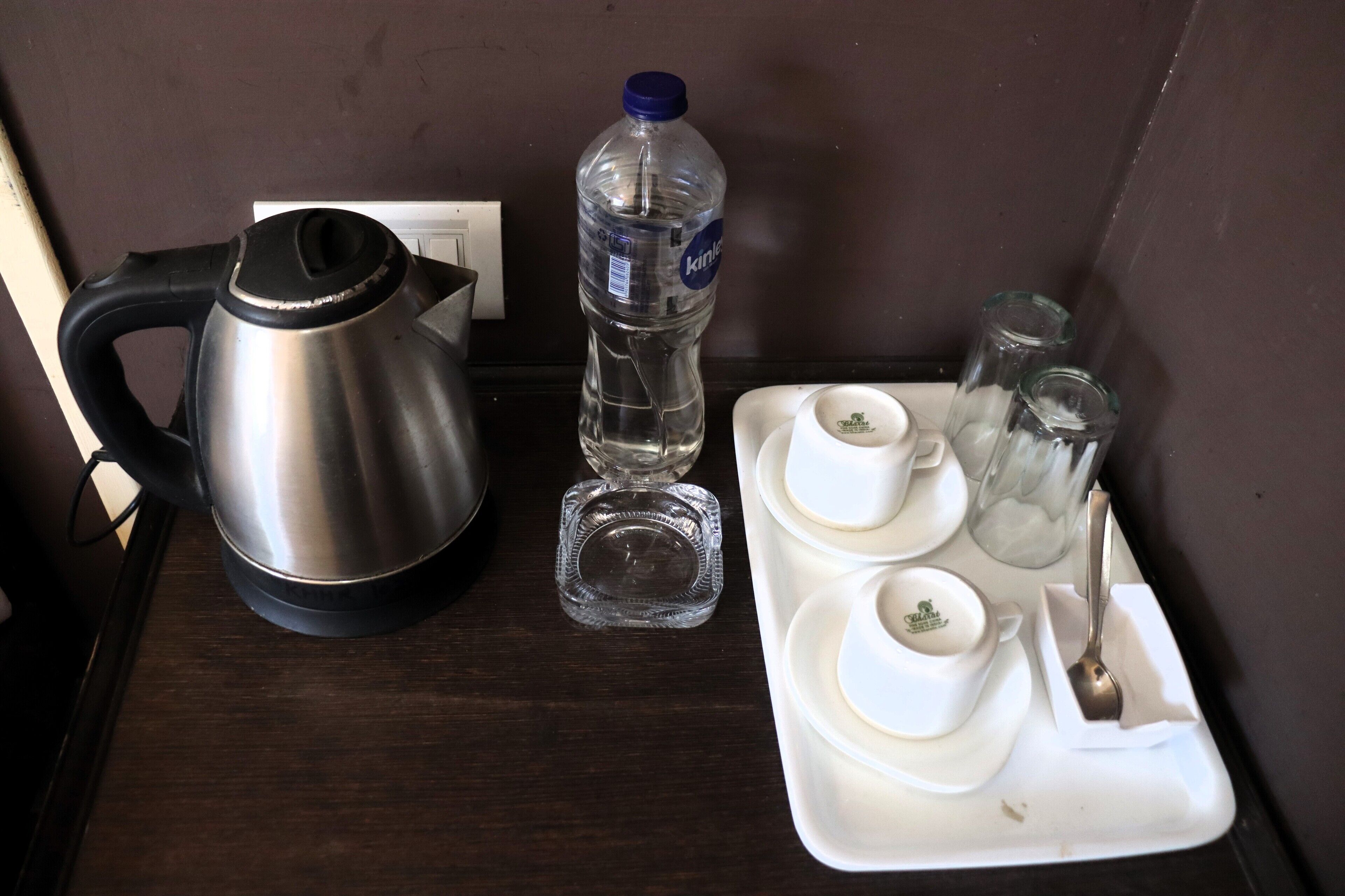 A kitchenette with a kettle, a bottle of water, and a tray with cups and a spoon.