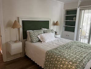 A neatly arranged bedroom with a bed, two bedside tables, a nightstand, a green headboard, and a window with blinds. - Sea Palms St Simons Island, GA Decorator furnished 2/2 island escape (St. Simons Island)