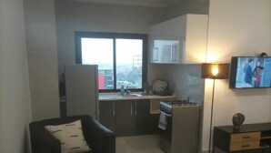 A modern kitchen with a large window, a dining area with a black sofa, and a TV on a stand. - Residence Holi (Abidjan)