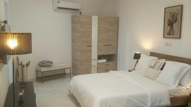 A bedroom with a bed, bedside tables, a wardrobe, and an air conditioning unit. - Residence Holi (Abidjan)