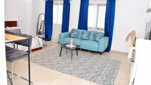 A modern hotel room with a bed, a blue sofa, a small table, and a mirror. - Residence Holi (Abidjan)