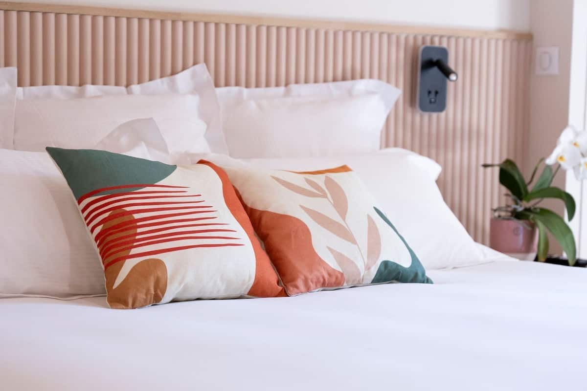 Una cama bien hecha con ropa blanca y almohadones decorativos.