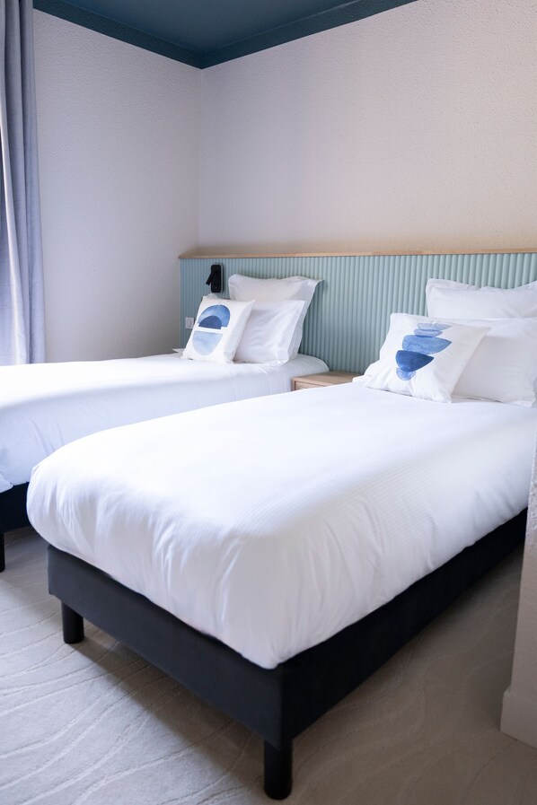 A hotel room with two single beds, a wooden nightstand, and a light blue headboard.