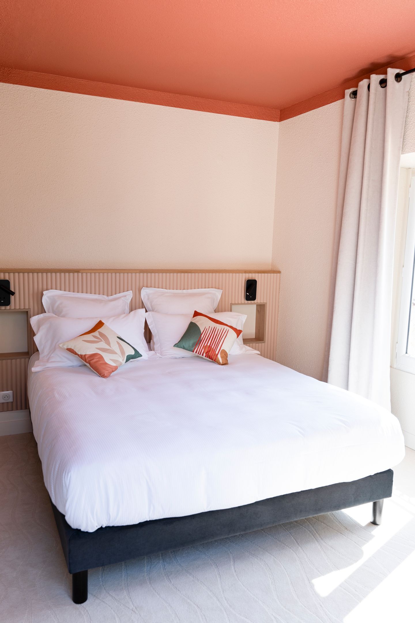 Een keurig opgemaakt bed met witte lakens en decoratieve kussens, een houten hoofdbord en een nachtkastje met een lamp.