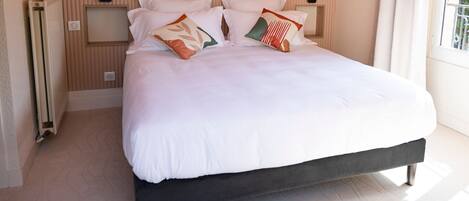 A neatly made bed with white bedding and decorative pillows, a wooden headboard, and a radiator on the left.