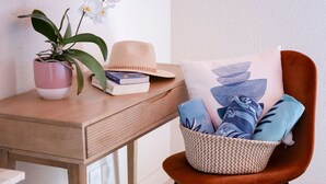 A wooden table with a potted orchid, a hat, and books. A wicker basket with pillows is on an orange chair. - La Bastide de Montferrat (Montferrat)