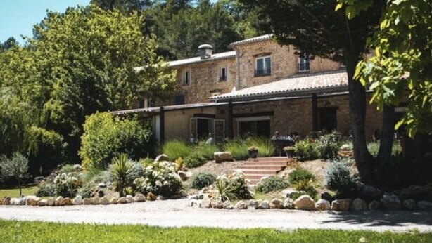 A stone house with a covered patio, surrounded by a landscaped garden with various plants and a gravel driveway. - La Bastide de Montferrat (Montferrat)