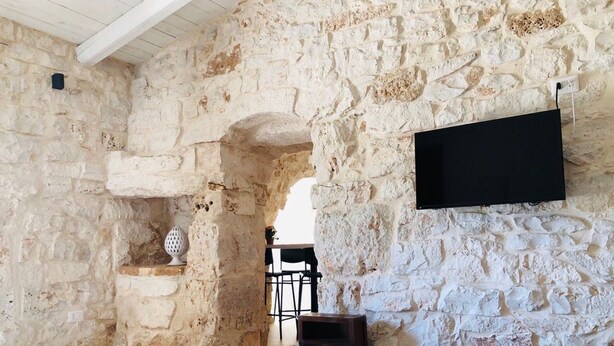 Quarto com paredes de pedra aparente, um banco de madeira, uma mesa pequena e uma televisão de tela plana fixada na parede.