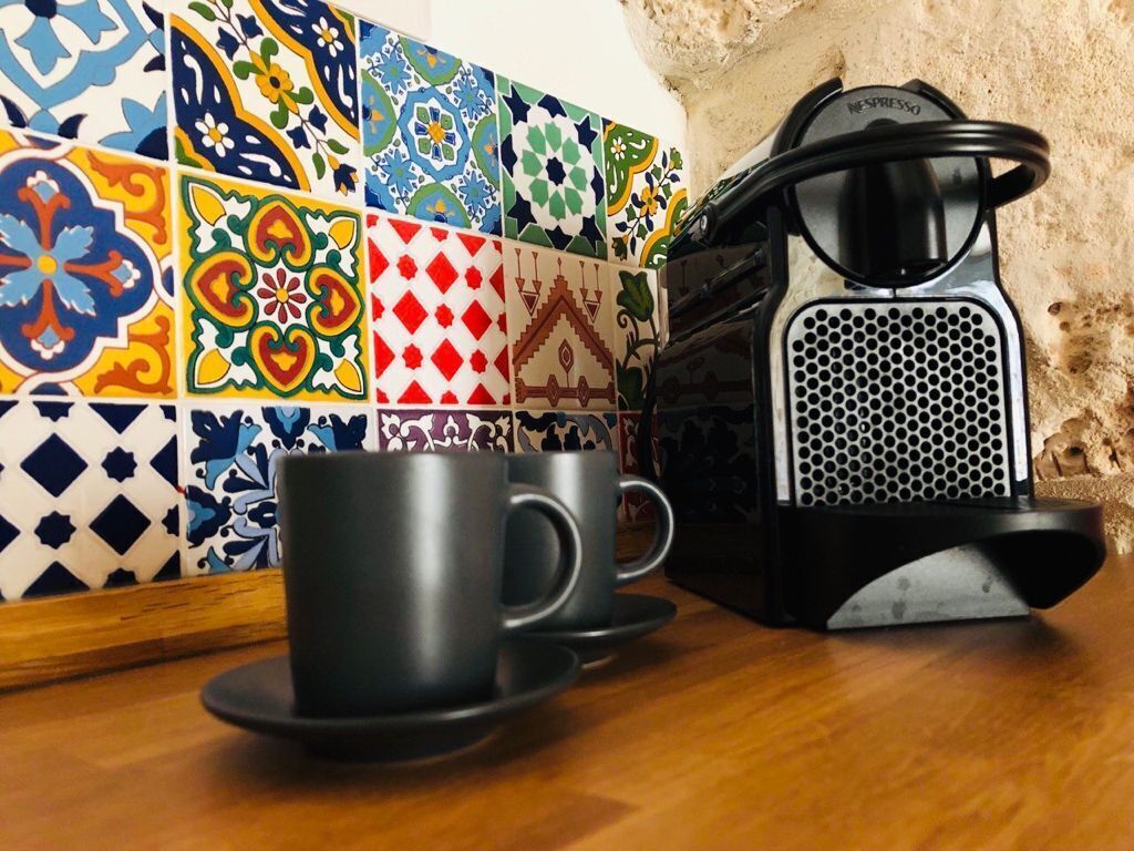 Una cucina con una macchina da caffè, due tazze nere e un vivace rivestimento in piastrelle.