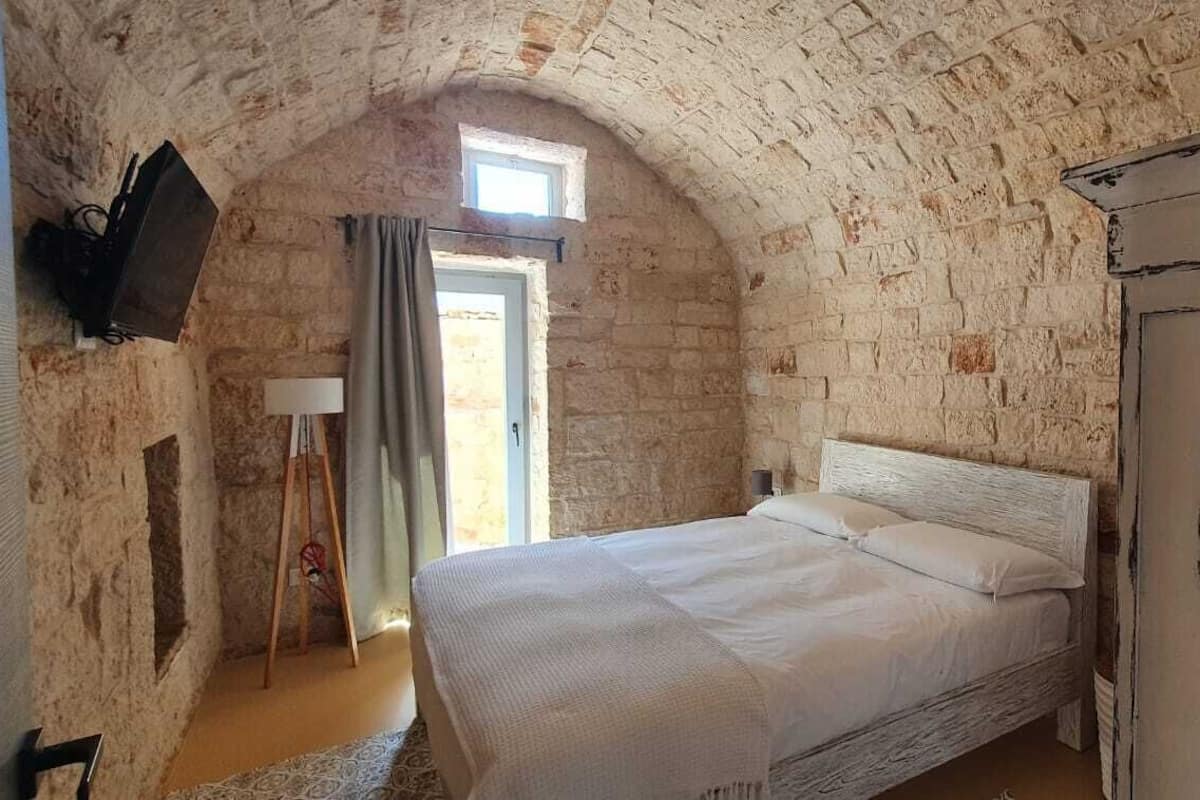 A bedroom with a stone wall, a bed, a window, and a door.