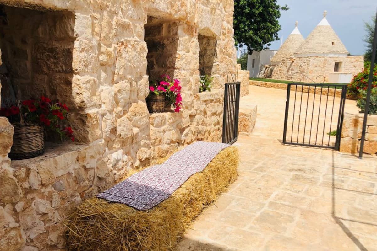 A stone building with a straw-covered bench, a basket with flowers, and a gate.