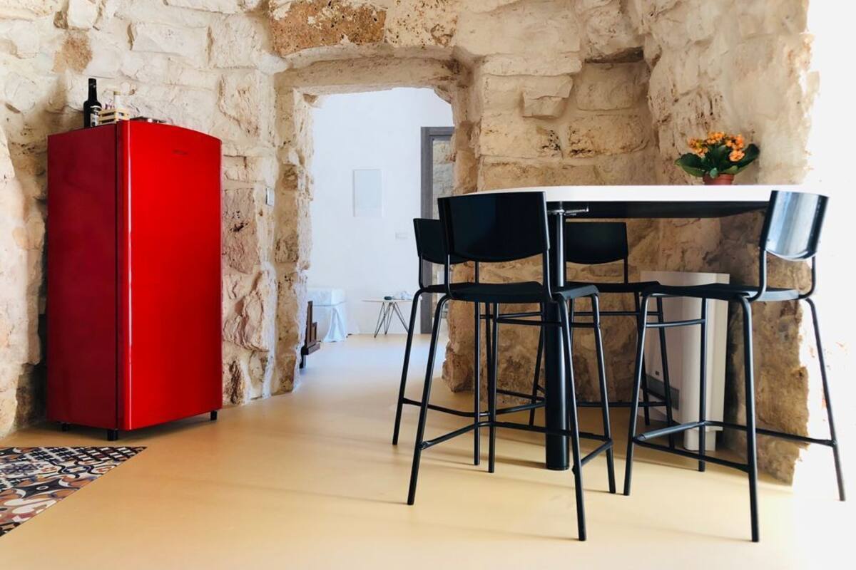 A stone-walled room with a red refrigerator, a table, and four black chairs.