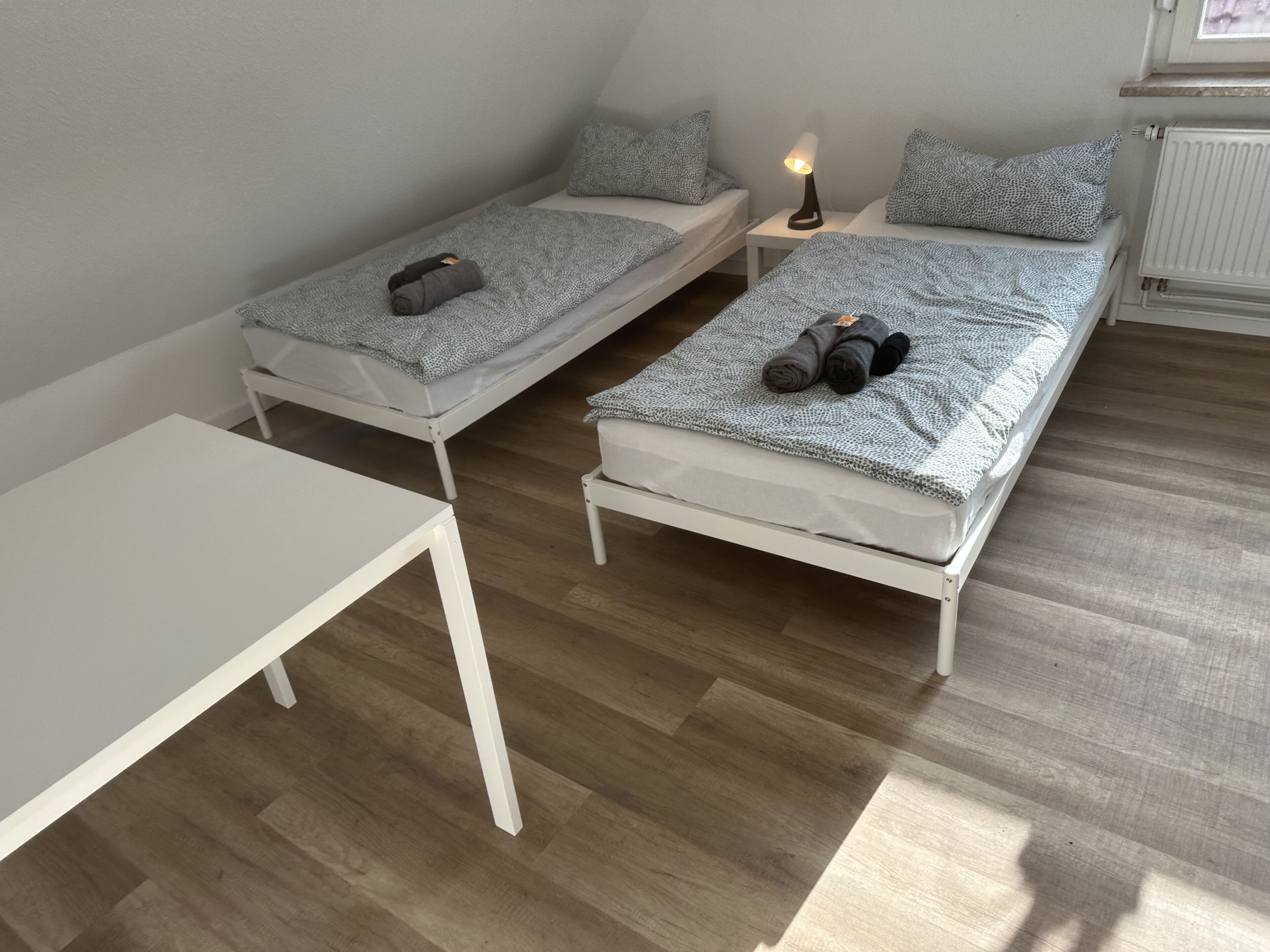 Une petite chambre propre, avec deux lits simples, une petite table et une table de chevet avec une lampe.