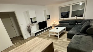 A modern living room with a flat-screen TV, a dark-colored sofa, and a white coffee table.