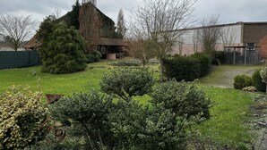 A garden with a gazebo, a large tree, and a brick building.