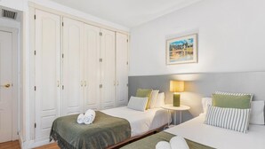 Ein Hotelzimmer mit zwei Betten, einem großen Kleiderschrank, einem Bild an der Wand und einer Nachttischlampe.