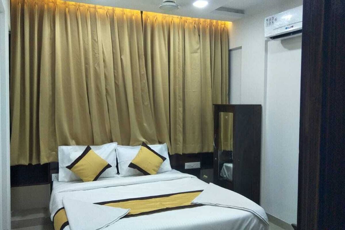 A hotel room with a bed, curtains, a mirror, and an air conditioning unit.