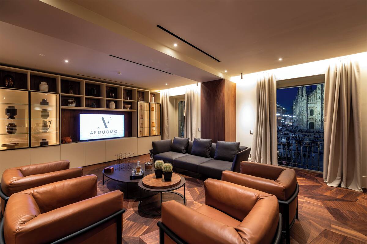 A modern living room with leather sofas, a coffee table, and a TV displaying 'AF DUOMO'.