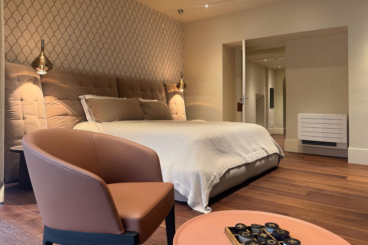 A modern bedroom with a tufted headboard, a leather chair, a wooden coffee table, and a patterned wall.