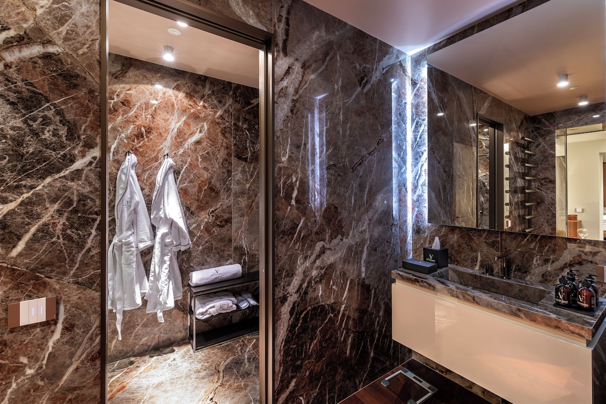 A modern bathroom with marble walls, a large mirror, and a vanity with a sink.