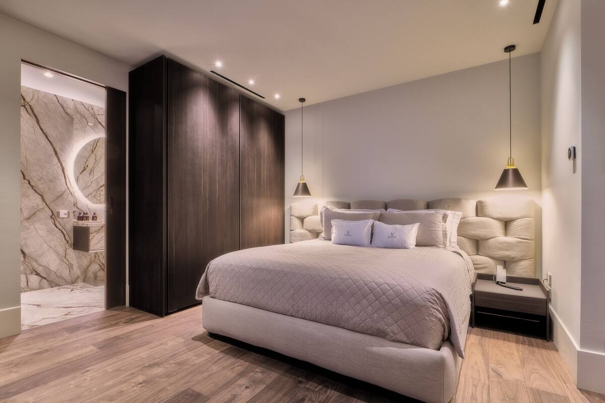A modern bedroom with a large bed, dark wood wardrobe, marble wall, and two bedside lamps.