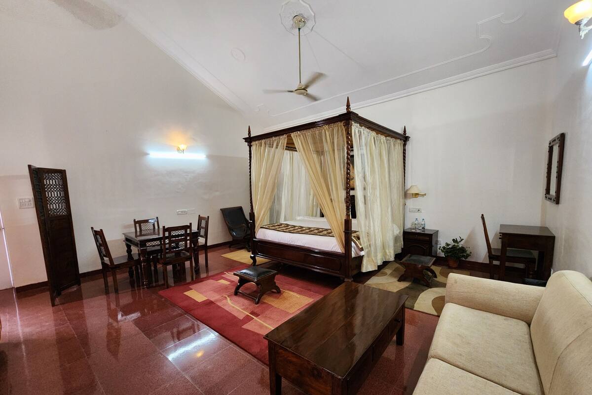 Una habitación amplia con una cama con dosel, una mesa de comedor con sillas, un sofá y un ventilador de techo.