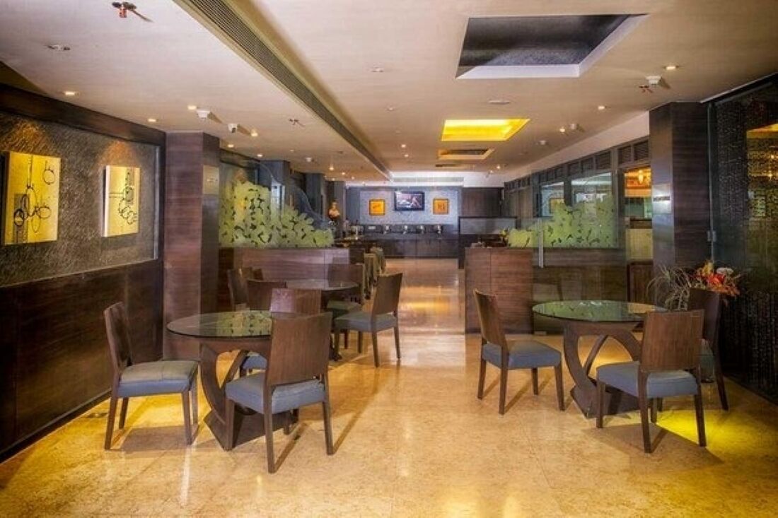 Un moderno vestíbulo de hotel con mesas y sillas redondas, una recepción y una gran pantalla de televisión.