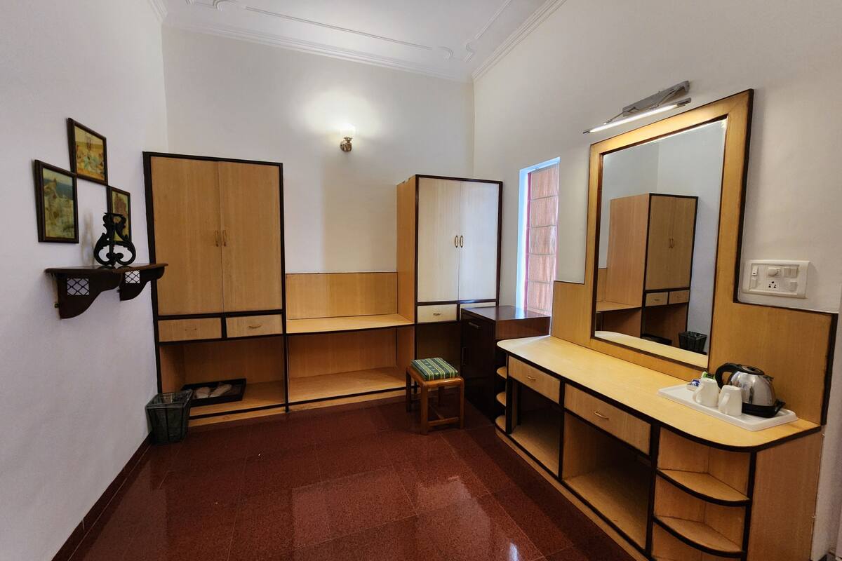 Una habitación de hotel con un armario de madera, un tocador con espejo, un taburete pequeño y un cubo de basura.