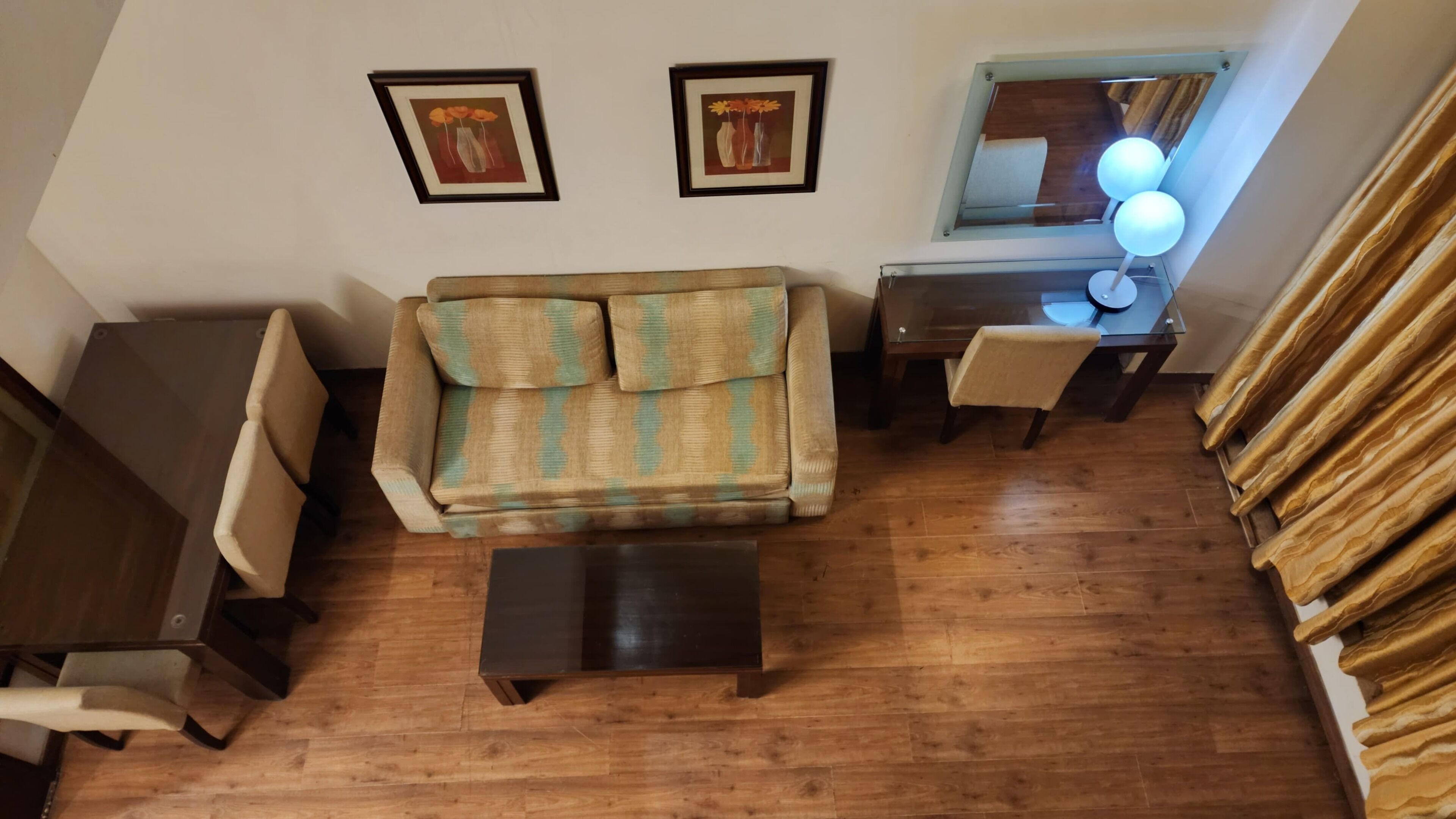 A living room with a sofa, a coffee table, a desk, and a chair. There are two framed pictures on the wall.