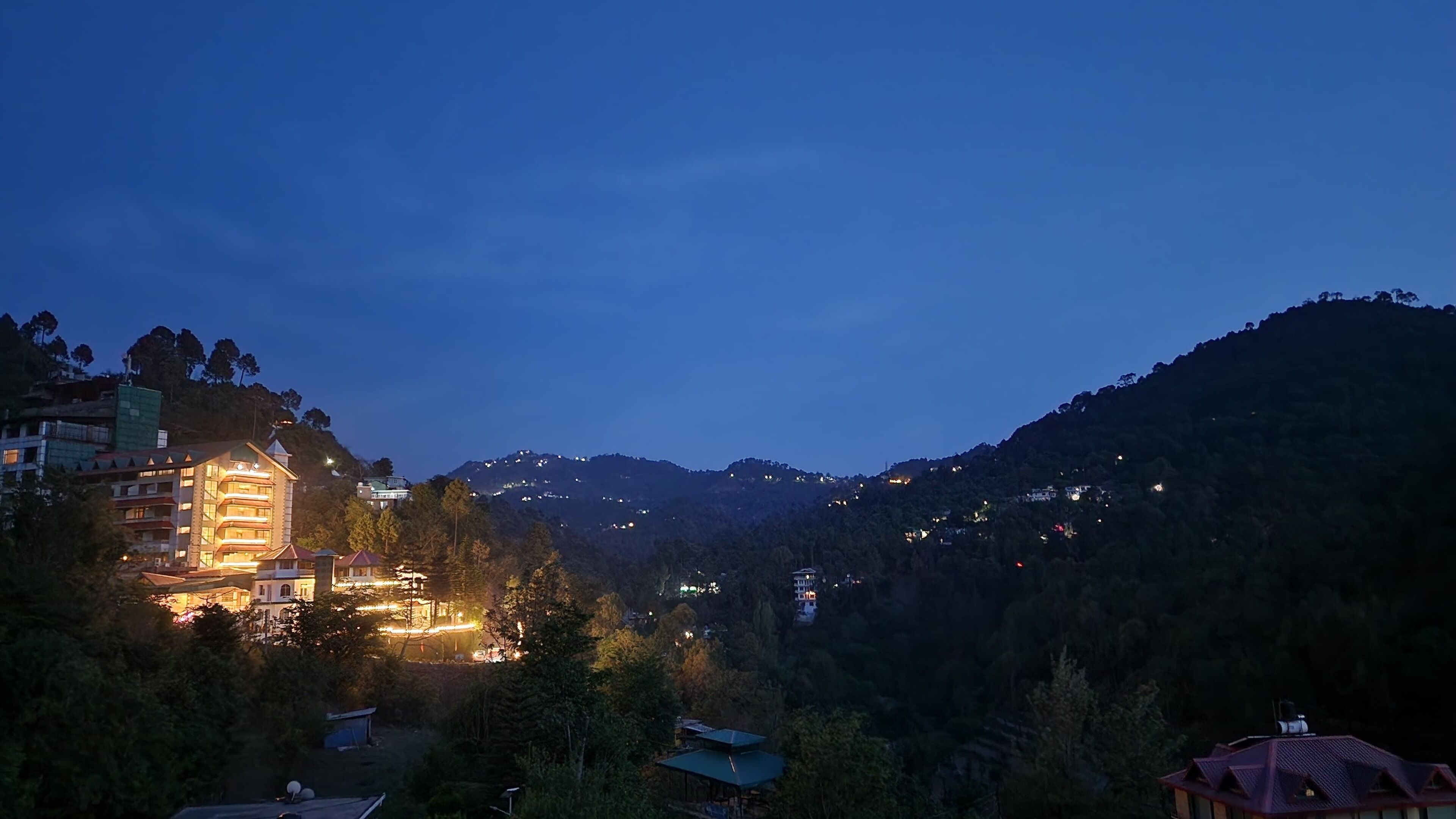A hotel with multiple floors, surrounded by lush greenery and hills in the background.